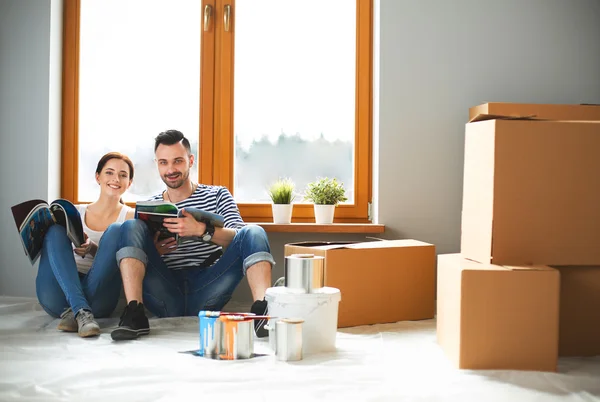 Atrakcyjna para siedzi na piętrze domu patrząc na dziennik i uśmiecha się do siebie. — Zdjęcie stockowe