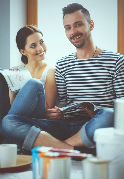 Attractive couple sitting on home floor looking at jurnal and smiling at each other.