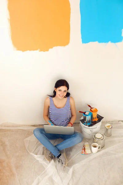 Retrato de mujer joven mientras pinta nuevo apartamento, sentado con el ordenador portátil — Foto de Stock