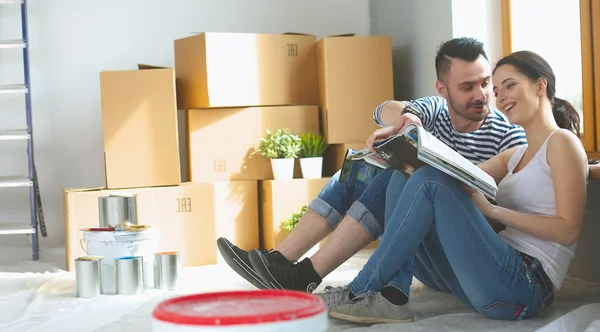 Attractive couple sitting on home floor looking at jurnal and smiling at each other. — Stock Photo, Image