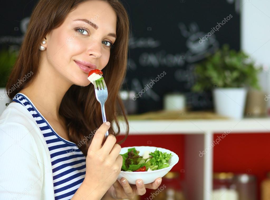 Mujer joven comiendo ensalada y sosteniendo una ensalada mixta
