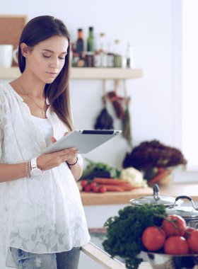 Mutfakta yemek yapmak için tablet bilgisayar kullanan genç bir kadın.