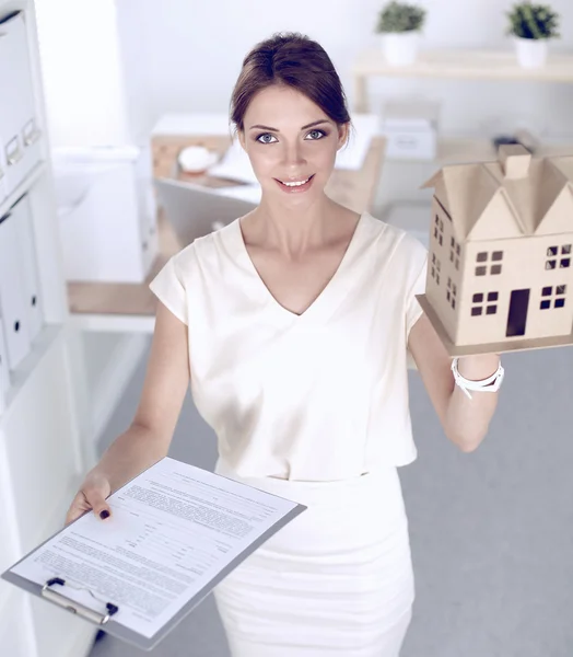 Retrato de una arquitecta sosteniendo una casita, de pie en la oficina —  Fotos de Stock