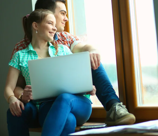 Portrait of young couple moving in new home sitting with laptop — Stock Photo, Image