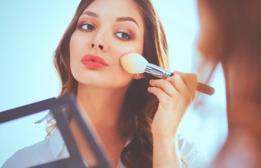 Genç ve güzel bir kadın aynanın yanında makyaj yapıyor.