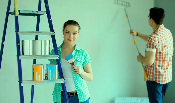 Retrato de feliz joven pareja sonriente pintando la pared interior de la nueva casa — Foto de Stock