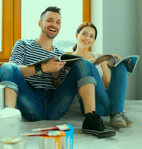 Attractive couple sitting on home floor looking at jurnal and smiling at each other. — Stock Photo, Image