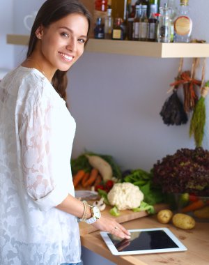 Mutfakta yemek yapmak için tablet bilgisayar kullanan genç bir kadın.