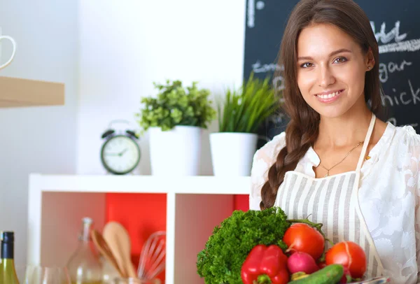 Souriante jeune femme tenant des légumes debout dans la cuisine — Photo