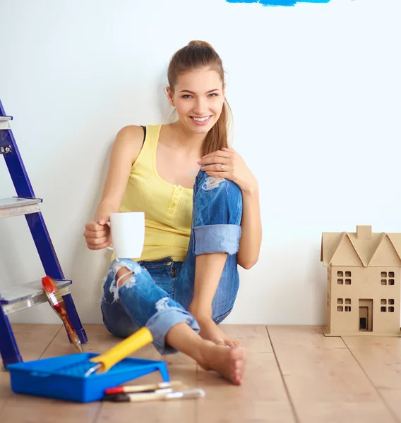 Porträtt av kvinnliga målare sitter på golvet nära väggen efter paintingand håller en kopp — Stockfoto