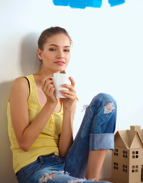 Portret van vrouwelijke schilder zittend op de vloer in de buurt van muur na paintingand holding een kop — Stockfoto