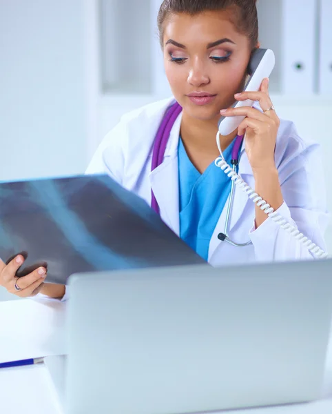 Vrouwelijke arts op zoek naar x-ray scan en praten over de telefoon in diagnostisch centrum, zittend aan het bureau — Stockfoto