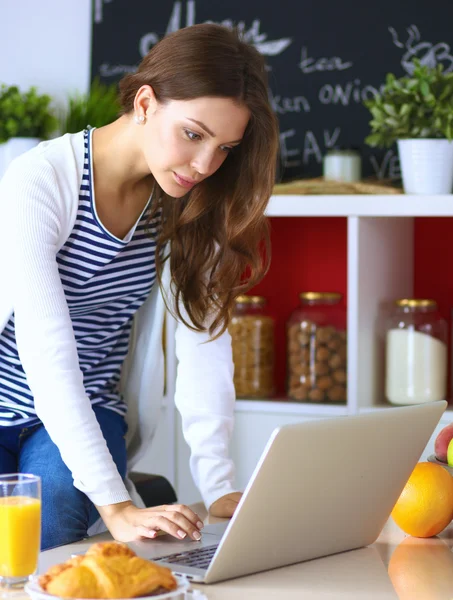 Attraente giovane donna che utilizza il computer portatile e seduto in cucina — Foto Stock