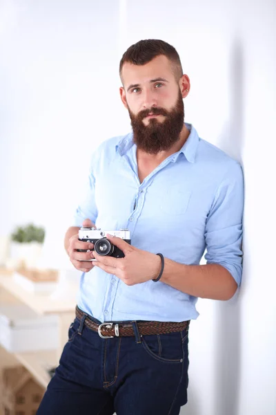 Joven barba hombre sosteniendo una cámara mientras está de pie sobre fondo blanco — Foto de Stock