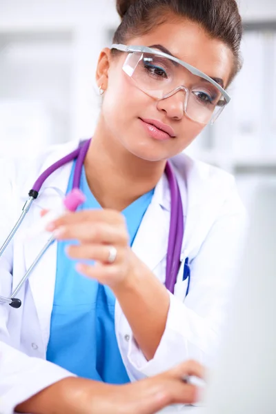 Hermosa joven sonriente doctora sentada en el escritorio y escribiendo. —  Fotos de Stock