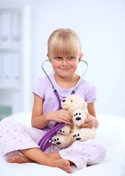 Klein meisje onderzoekt haar teddybeer met stethoscoop. — Stockfoto