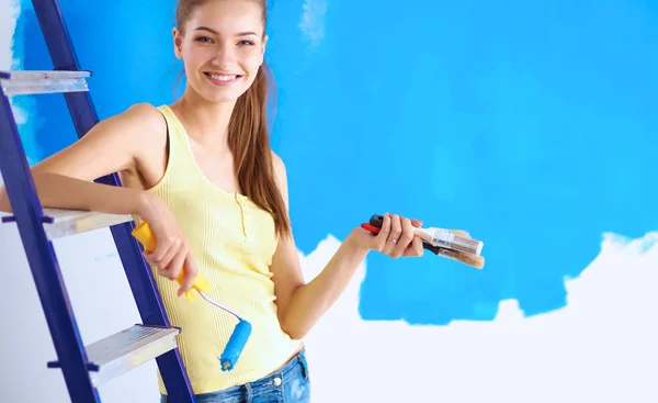 Gelukkig mooie jonge vrouw doet wandschildering, zittend op de ladder — Stockfoto