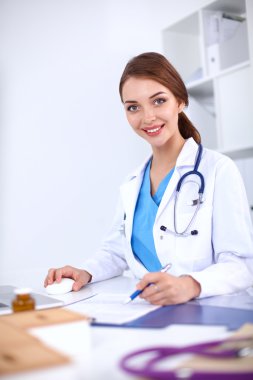 Güzel, genç, gülümseyen bayan doktor masada oturuyor ve yazıyor..