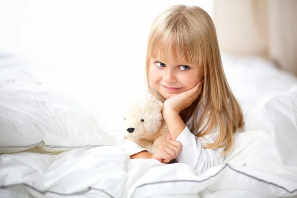 Niña con osito de peluche acostado en la cama en casa — Foto de Stock
