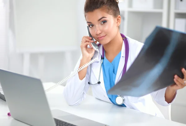 Jonge vrouwelijke arts studeert röntgenfoto zittend op het bureau — Stockfoto