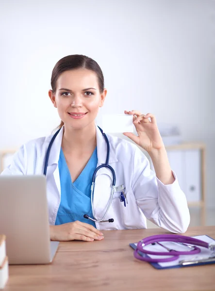 Schöne junge lächelnde Ärztin sitzt am Schreibtisch und schreibt. — Stockfoto