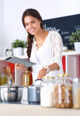 Mutfakta yemek yapmak için tablet bilgisayar kullanan genç bir kadın.