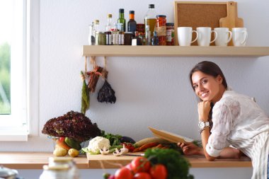 Mutfakta yemek kitabı okuyan genç bir kadın yemek tarifi arıyor.