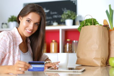 Gülümseyen kadın mutfakta tablet ve kredi kartı kullanarak alışveriş online