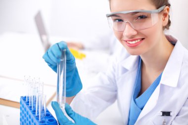 Kadın araştırmacı, beyaz arka planda izole edilmiş ilaç şişeleri ve mataralarla çevrili.