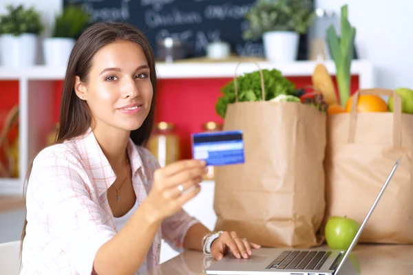 Usmívající se žena online nakupování pomocí tabletu a kreditních karet v kuchyni — Stock fotografie