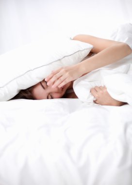 Kadın yatakta uzanıyor ve kulaklarını yastıkla kapatıyor.