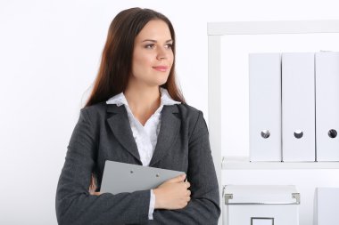 Çekici genç iş kadını masanın yanında elinde dosyayla duruyor.