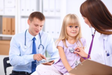 Kadın doktor ameliyatta steteskopla çocuğu muayene ediyor.