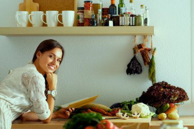 Mutfakta yemek kitabı okuyan genç bir kadın yemek tarifi arıyor.