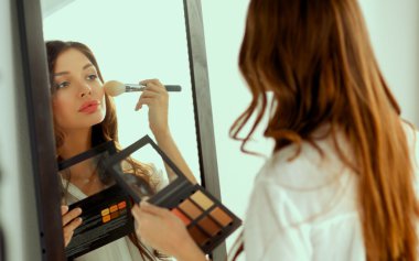 Genç ve güzel bir kadın aynanın yanında makyaj yapıyor.