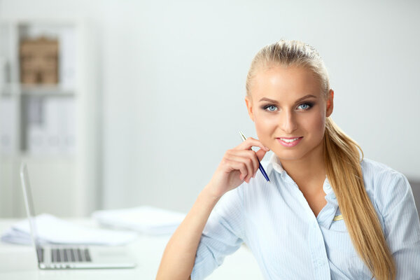 Attractive businesswoman sitting on a desk with laptop in the office