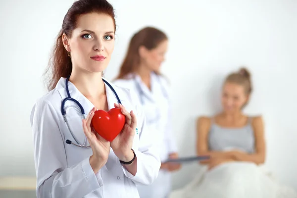 Young woman doctor holding a red heart, standing on gray background — Stock Photo, Image