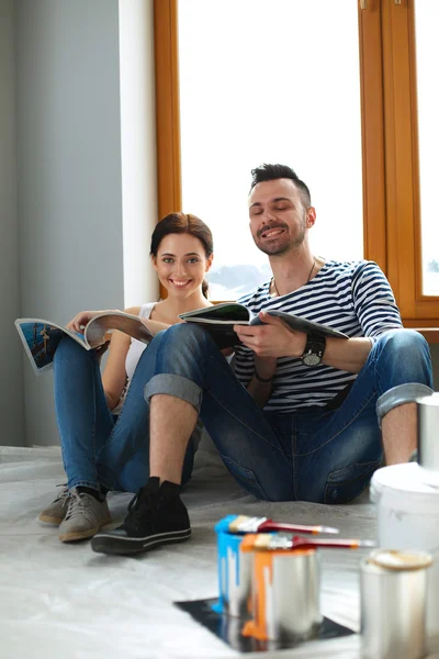 Atraktivní pár na domácí podlahy při pohledu na časopis a usmívá se na sebe. — Stock fotografie