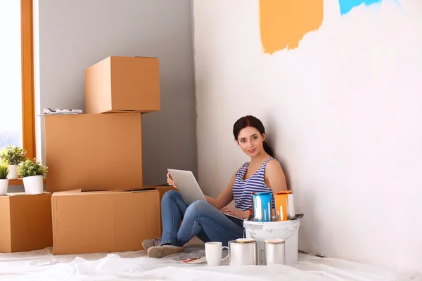 Portret młodej kobiety podczas malowania nowe mieszkanie, siedząca z laptopem — Zdjęcie stockowe