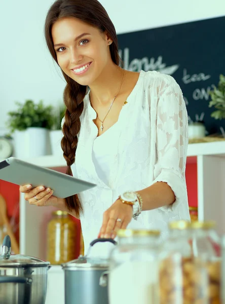 Jovem usando um computador tablet para cozinhar em sua cozinha — Fotografia de Stock