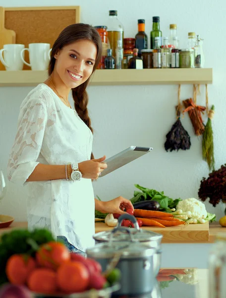 Jovem usando um computador tablet para cozinhar em sua cozinha — Fotografia de Stock