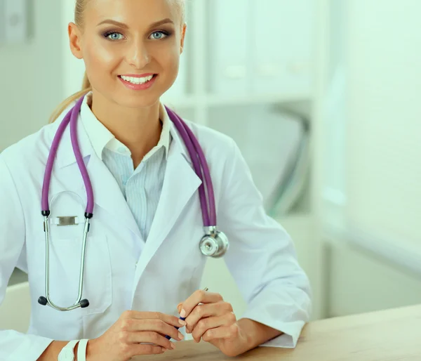 Beautiful young smiling female doctor sitting at the desk and writing. — Stock Photo, Image