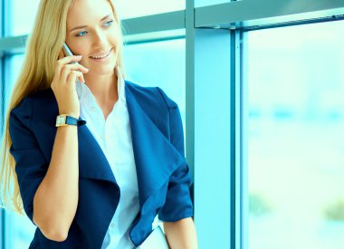 İş kadını ofis penceresinin önünde cep telefonuyla konuşuyor