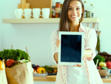 Mutfakta yemek yapmak için tablet bilgisayar kullanan genç bir kadın.