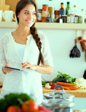 Mutfakta yemek yapmak için tablet bilgisayar kullanan genç bir kadın.