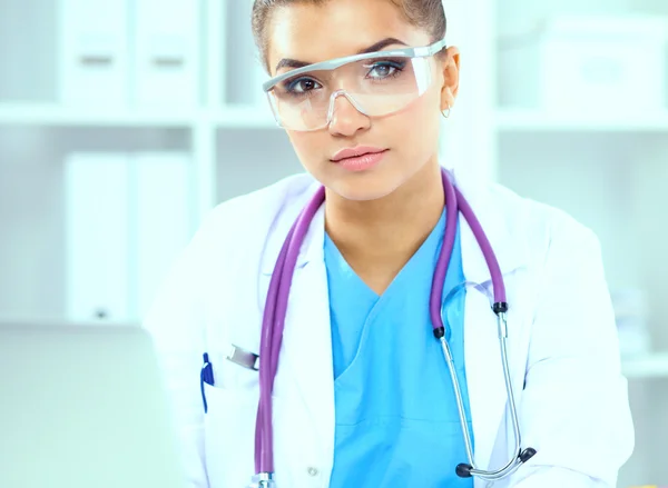 Hermosa joven sonriente doctora sentada en el escritorio y escribiendo. — Foto de Stock