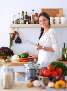 Mutfakta yemek yapmak için tablet bilgisayar kullanan genç bir kadın. .