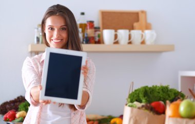 Mutfakta yemek yapmak için tablet bilgisayar kullanan genç bir kadın. .