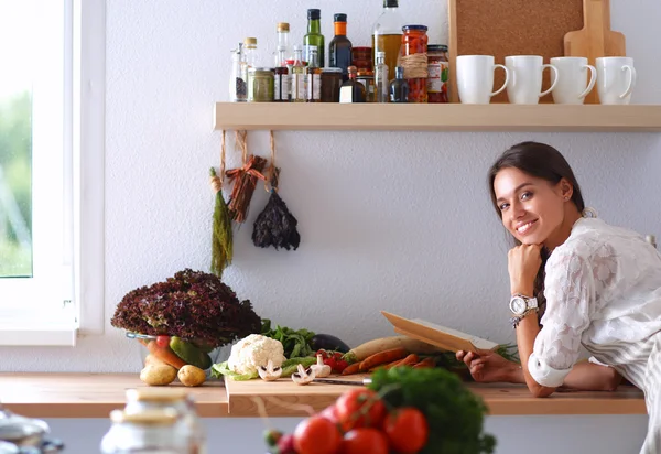 Jovem mulher lendo livro de receitas na cozinha, à procura de receita — Fotografia de Stock