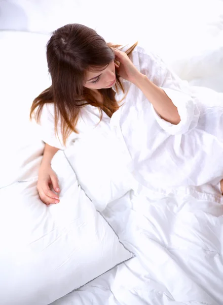 Ung kvinna med en kudde medan du sitter på sin säng — Stockfoto